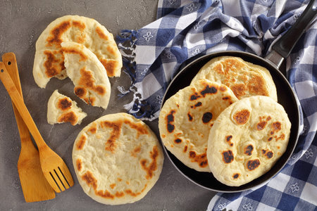 close-up of freshly fried pita bread in skillet with kitchen towel and wooden spatulas on concrete...