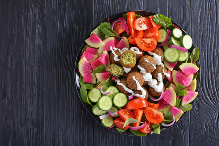 delicious falafel balls on platter with vegetable colorful salad of watermelon radish, chard leaves, cucumber and tomato slices, healthy eating concept, view from aboveの写真素材