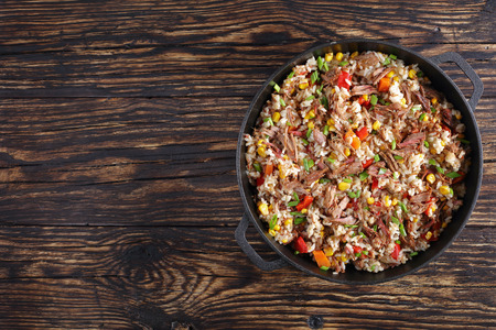 delicious shredded juicy Beef mixed with rice, vegetables, corn kernels, sweet pepper pieces, spices and sprinkled with green onion in cast iron pan on wooden table, horizontal view from aboveの写真素材