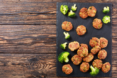 delicious baked chicken broccoli meatballs with grated cheese, and spices on black slate tray on wooden table, healthy low calories recipe, view from above, blank space for text leftの写真素材
