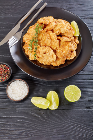 delicious crispy bite-sized deep fried morsels of veal brain served on black plate on wooden table with peppercorns, lemon slices, salt at background,  vertical view from above, close-upの写真素材