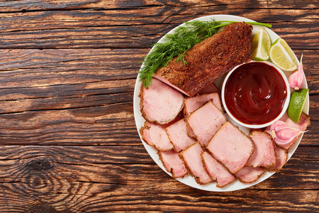 delicious sliced ham seasoned with ground spices with barbecue sauce, lime slices, garlic and dill served on white plate on rustic wooden table, view from aboveの写真素材