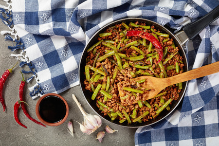 Szechuan Pork Stir Fry with Green Beans in a skillet on concrete table with soy sauce and dried chili peppers,  view from above, close up, flat layの写真素材