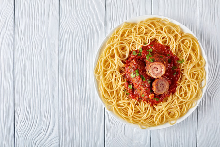 Italian Braciole served with spaghetti - beef steak rolls filled with sliced prosciutto, grated parmesan cheese and parsley with marinara sauce on a white plate, view from above, flat layの写真素材