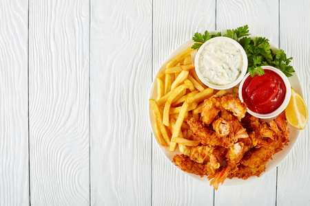 delicious crunchy corn flakes breaded and deep-fried shrimps on a plate on a wooden table with french fries, ketchup and coctail sauce in bowls  view from above, close-up, flat layの写真素材