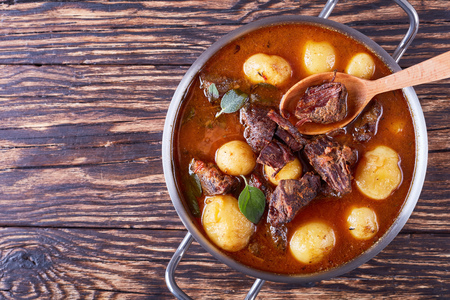 hot Beef Stew with tender cubes of meat, whole new potatoes, carrots and herbs in a metal casserole on old rustic wooden table, irish cuisine, horizontal view from above, flatlayの写真素材