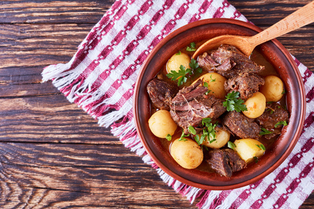 hot Beef Stew with tender cubes of meat, whole new potatoes, onion and herbs in a clay bowl on old rustic wooden table with napkin, irish cuisine, horizontal view from above, flatlayの写真素材