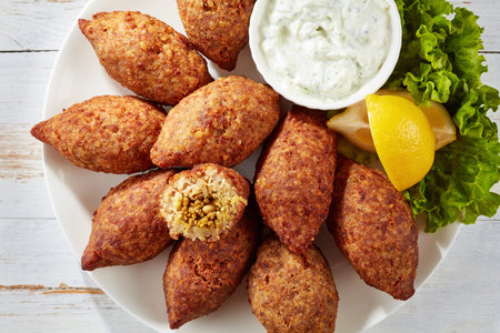delicious fried kibbeh with yogurt sauce in a bowl served on a white plate with lettuce and lemon...