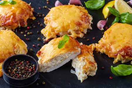 close-up of  Pork Chops Topped with finely chopped Onions, Mayo and melted Cheese on a black slate plate on a wooden table, horizontal view from aboveの写真素材
