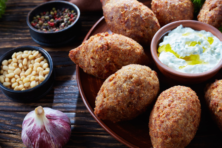 close-up of deep fried kibbeh of ground beef meat mixed with bulgur, stuffed with fried minced meat with pine nuts, spices, garlic and herbs on a clay plate on an old dark wooden tableの写真素材