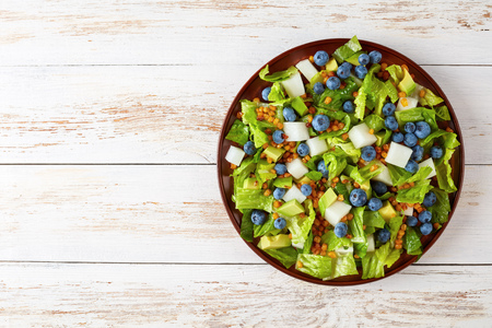 Mexican Salad with Blueberries, jicama, roasted Corn kernels and Avocado on a clay plate on a rustic wooden table, view from aboveの写真素材