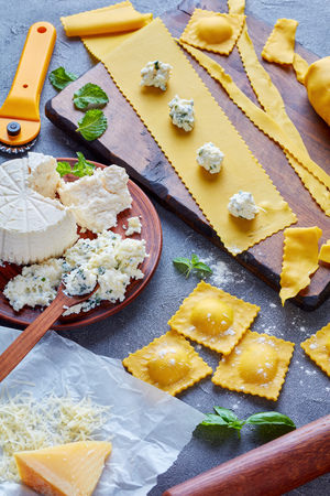cooking up delicious ravioli with ricotta cheese filling mixed with finely chopped mint and basil leaves on a concrete kitchen table, vertical view from aboveの写真素材