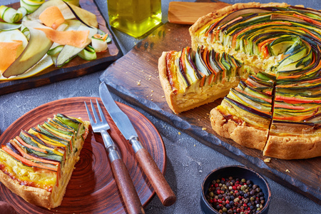 close-up of sliced Spiral tart with zucchini, eggplant, carrot strips in ricotta cheese filling, served on a clay plate with fork and knife, view from aboveの写真素材