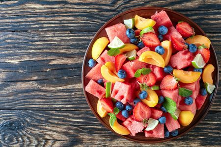 delicious colorful summer watermelon salad with blueberries, peach slices, strawberry and lime on a clay plate on an old rustic table, horizontal view from above, flatlayの写真素材