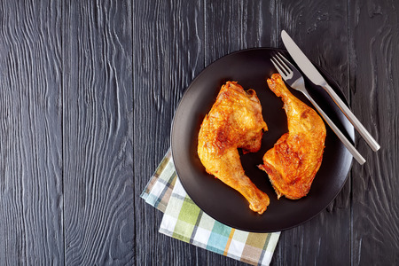 fried chicken legs with golden crispy skin served on a black plate  with fork and knife on a wooden table, view from above, flatlayの写真素材