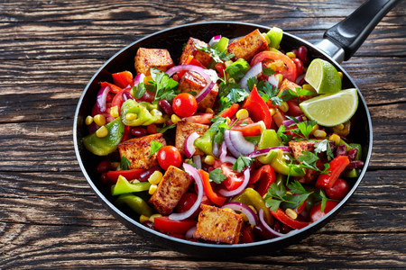 Delicious Cowboy Caviar cooked from colorful, fresh vegetables: green and red pepper, black beans, sweet corn, tomato, red onion, tofu cheese, garnished with parsley leaves, on a black skilletの写真素材