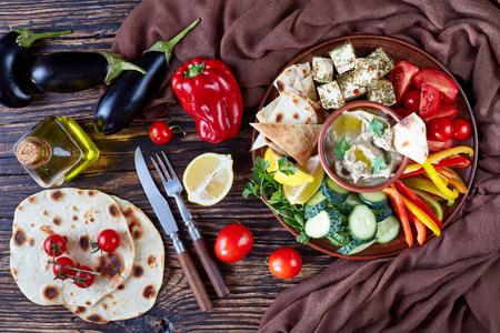Traditional Baba ganoush: baked eggplant with lemon juice, garlic, olive oil, tahini paste in the plate with fresh vegetables, tosted pita, spiced cheese on the wooden table with ingredients, top viewの写真素材