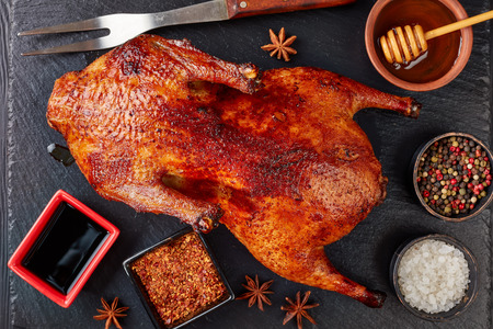 close-up of whole Amber-Hued grilled duck with extremely crispy flavour skin on a black slate tray with spices and fork, view from above, flatlayの写真素材