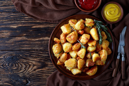 overhead view of crispy Roast Potatoes with spices and rosemary served on a clay dish with mustard and tomato sauce on an old wooden table, view from aboveの写真素材