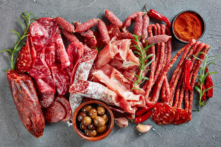 a set of spanish sausages and dry cured meat - jamon, chistorra, chorizo, salchichon, fuet, olives, rosemary, chili peppers on a grey concrete table, view from above, flatlay, close-upの写真素材