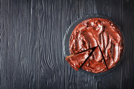 sliced chocolate Cake with apricot jam filling topped with Chocolate Ganache  on a stone plate on a black wooden table, horizontal view from above, flatlay, copy spaceの写真素材