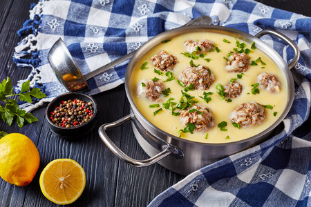 close-up of classic Greek Meatball Soup - Giouvarlakia, Youvarlakia in Egg lemon sauce in a metal casserole on a wooden table with kitchen towel and ladle, view from aboveの写真素材
