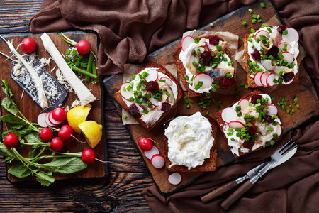 Smorrebrod - danish open faced sandwiches with smoked mackerel slices, cream mixed with grated horseradish, beetroot, fresh radish, onion on a dark cutting board,  flatlayの写真素材