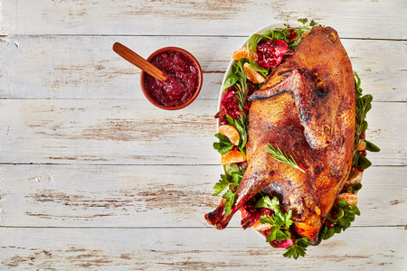 overhead view of a whole roasted free-range turkey on a white oval plate with greens, pomegranates and tangerines, view from above, rustic styleの写真素材