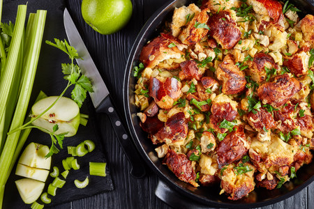classic version of thanksgiving or christmas Stuffing, made with bread, celery, onions, apples, chestnuts, thyme and sage in a black casserole with ingredients on a table, close-upの写真素材