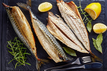 close-up of smoked mackerel served on a black slate tray with salt, peppercorn, rosemary and lemon slices, fork and knife, view from above, flatlayの写真素材