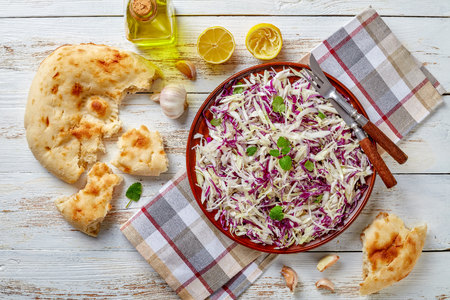overhead view of Lebanese Cabbage salad with lemon juice, olive oil, garlic, dried and fresh mint in an earthenware bowl on a napkin with pita bread on a table, horizontal view from above, close-upの写真素材