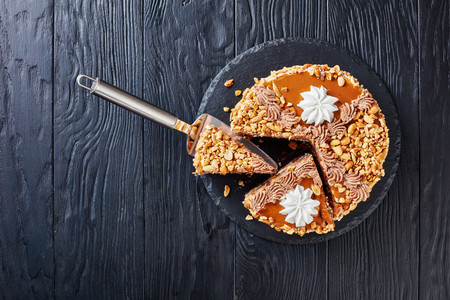 peanut cake topped with cocoa peanut butter cream and egg whites roses cut in slices on a stone plate on a wooden table, view from above, close-up, flatlayの写真素材