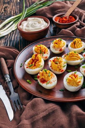 Deviled Eggs sprinkled with paprika and finely chopped green onion on a clay plate on an old rustic...