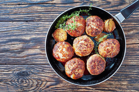 homemade fried meat cutlets, patties of chopped meat in a skillet with thyme, garlic and onion on an old wooden table, view from above, close-upの写真素材