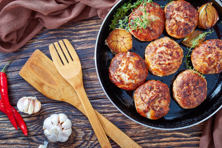 homemade fried meat cutlets, patties, turkey meat cakes of chopped meat in a skillet with thyme, garlic and onion on an old wooden table with brown cloth, view from above, close-upの写真素材