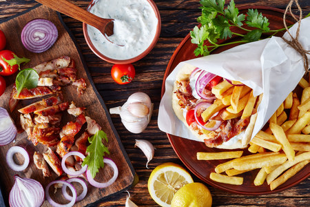 greek souvlaki, pita ma gyros with chicken meat, vegetables, french fries and yogurt garlic sauce, ingredients on a cutting board on a rustic table, view from above, flatlayの写真素材