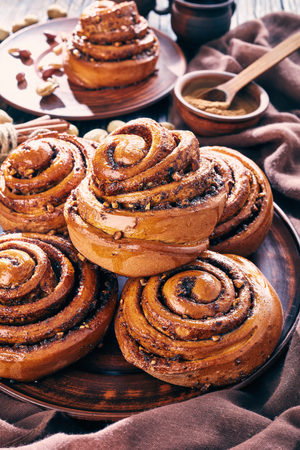 freshly baked Cinnamon rolls buns with peanuts served on a earthenware plate and two cups of coffee on an old wooden table. Kanelbulle swedish dessert, vertical view from above, close-up, macroの写真素材