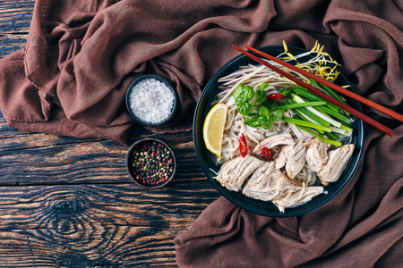 overhead view of vietnamese soup Pho Ga with chicken, rice noodles, bean sprouts, fresh herbs in a...