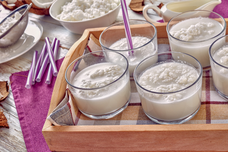 homemade coconut cocktail of coconut water, coconut milk and cream in the glass cups on a wooden tray with ingredients on a white wooden table, close-upの写真素材