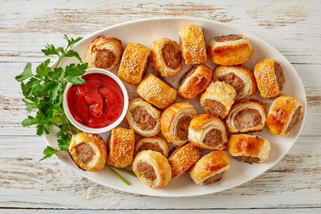 sausage rolls on a white oval platter with tomato sauce on a wooden rustic table, finger food, english cuisine, view from above, close-upの写真素材