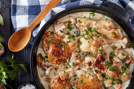 chicken fricassee in a black dutch oven - chicken meat browned and braised in white wine creamy sauce with mushrooms and vegetables, classic french recipe, view from above, flat lay, close-upの写真素材