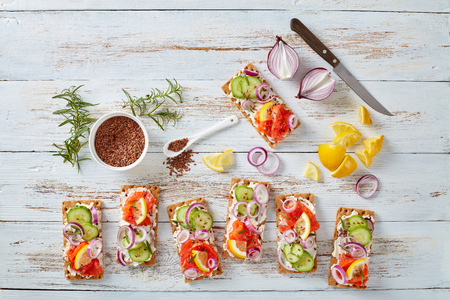 Thin Sourdough Rye Crispbread salmon open sandwiches with cucumber, cream cheese and red onion,  sprinkled with flax seeds on a white old wooden table, healthy lifestyle diet, view from above, flatlayの写真素材