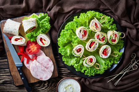 sliced sandwich wraps on a skewers on a plate. ingredients and garlic sour cream sauce in a bowl on a rustic wooden table with brown cloth, view fronm above, flatlayの写真素材