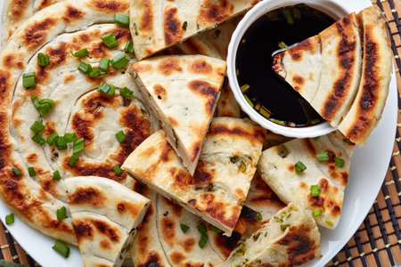 Freshly fried Chinese green onion Pancakes on a platter with soy sauce horizontal view from above,...