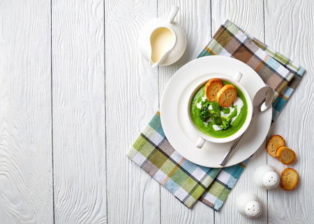 broccoli cream soup in a white soup bowl served with toasted slices of baguette and fresh cream, view from above, flatlay, copy spaceの写真素材