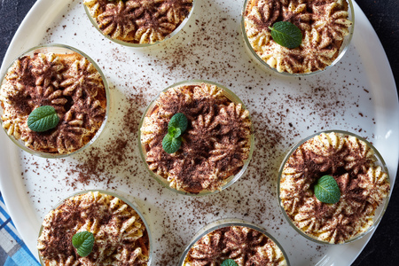 classic tiramisu, italian dessert of savoiardi biscuits, egg, sugar, coffee, mascarpone cheese in round glasses on a platter, horizontal view from above, flat lay, close-up, macroの写真素材