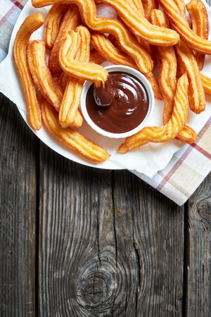 churros - Traditional Spanish and Mexican dessert on a white plate with chocolate sauce on an old grey rustic wooden table, vertical view from aboveの写真素材