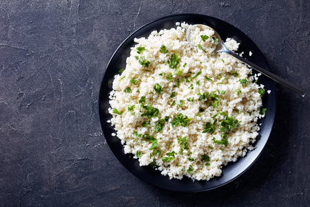 close-up of Cauliflower rice or couscous mixed with finely chopped parsley in a black bowl on a concrete table, horizontal view from above, flatlayの写真素材
