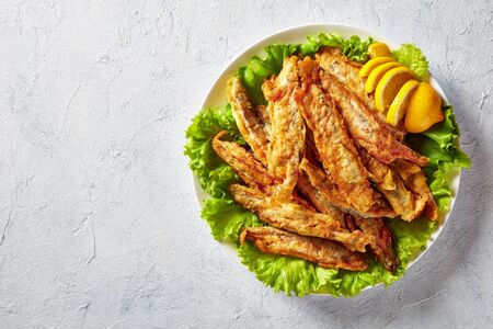 Fried in batter capelins served on a bed of fresh lettuce leaves with sliced lemon on a plate on a concrete table, view from above, copy space, close-upの写真素材