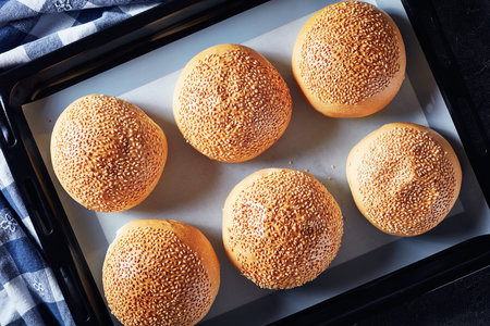 Freshly baked hot homemade burger buns on a baking pan, view from above, flatlay, close-up